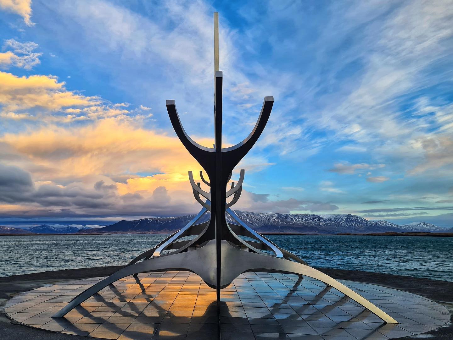 The Sun Voyager sculpture in Reykjavík by the sea, with mountains and a colorful sky in the background.