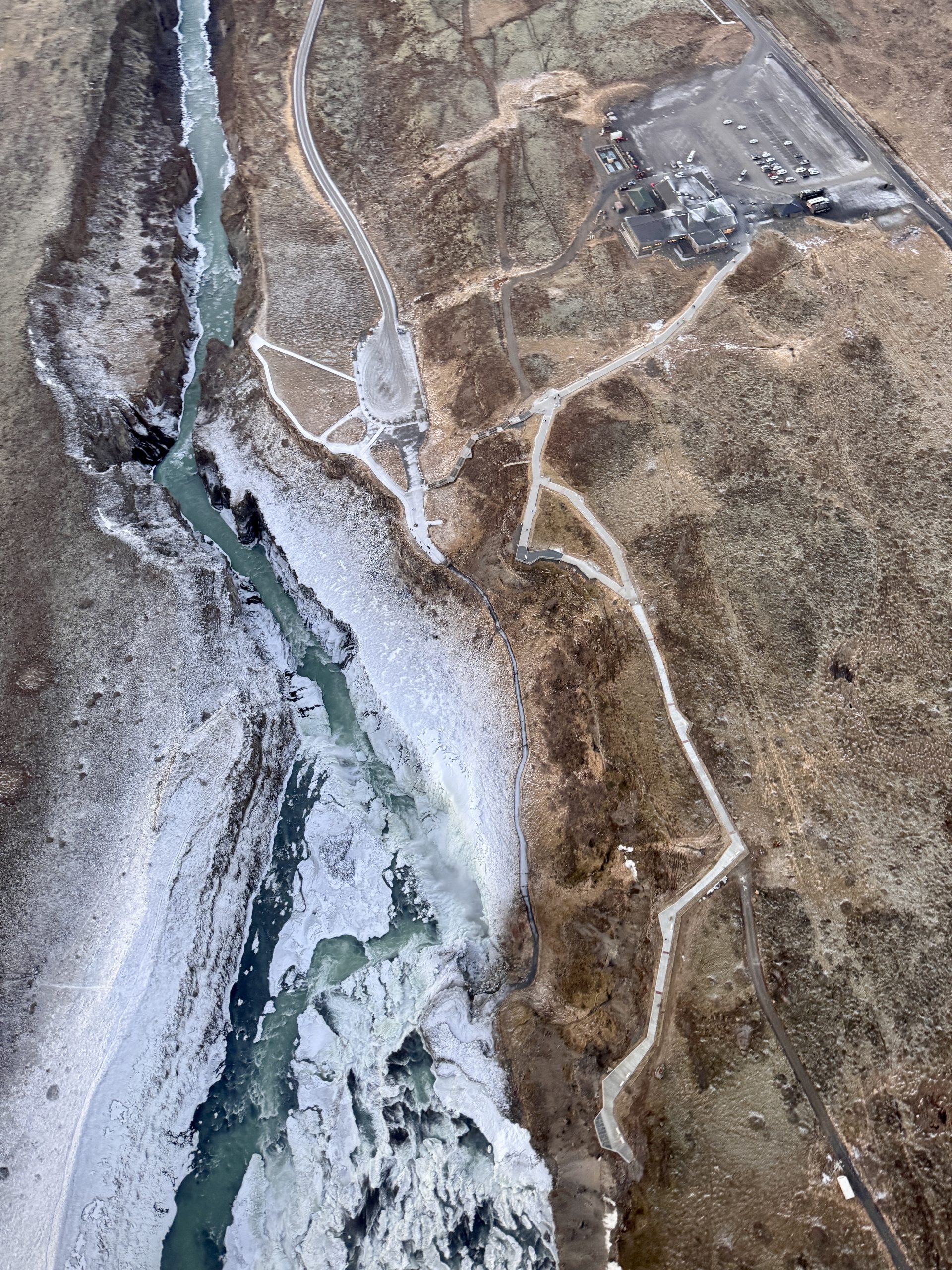 Aerial view of Gullfoss waterfall in Iceland, with a glacial river flowing through a deep canyon, seen from a private helicopter.